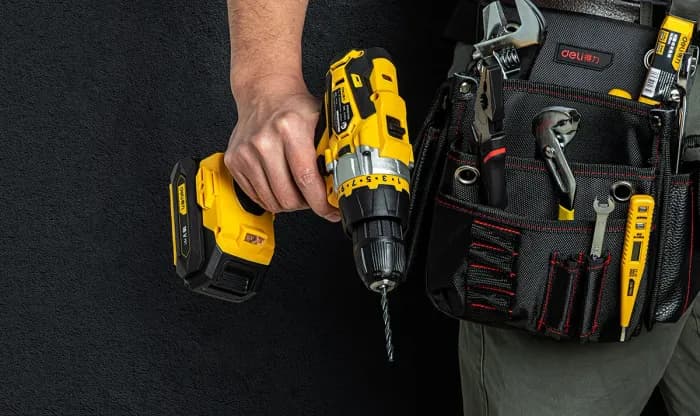 Hand holding a yellow and black drill with a tool belt.